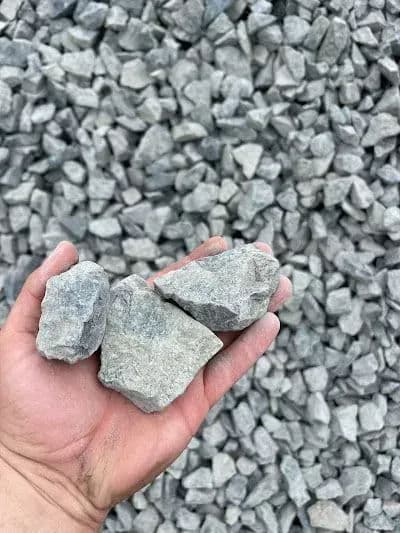 Hand holding three gray gravel stones against a background of gravel pile.