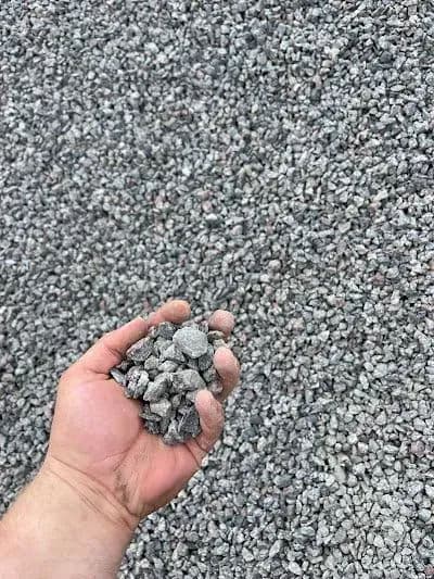 Hand holding gravel against a backdrop of loose gravel, showcasing texture and size.