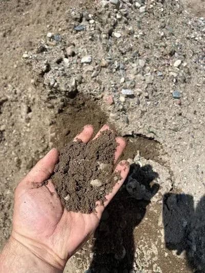 Hand holding loose soil with gravel in a construction site background.