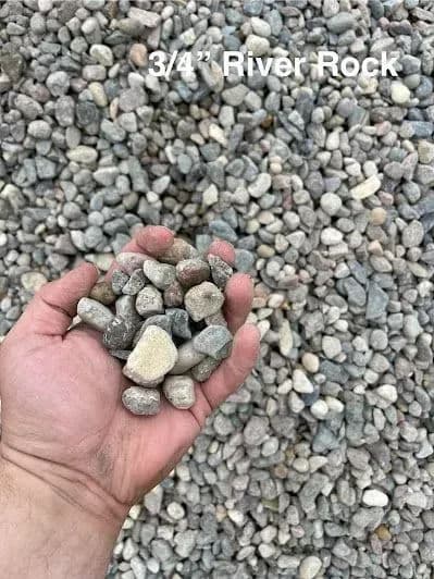 Hand holding 3/4" river rock with gravel background for landscaping and decorative use.