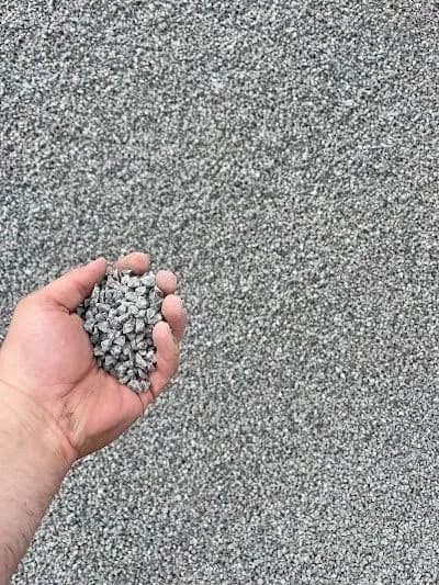 Hand holding gray construction gravel against a gravel background for landscaping or building.