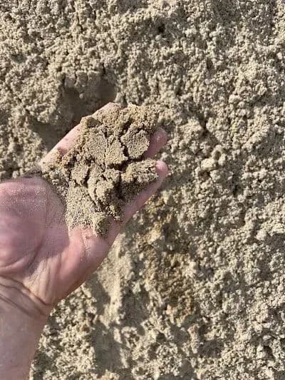 Hand holding sand against a sandy background, showcasing texture and color.