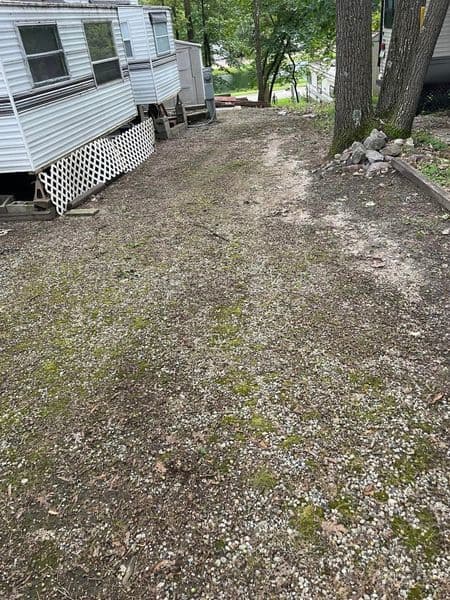 Gravel pathway between mobile homes in a wooded area, featuring greenery and trees.