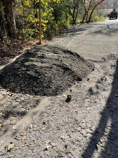 Pile of gravel on a gravel road surrounded by trees and autumn foliage.