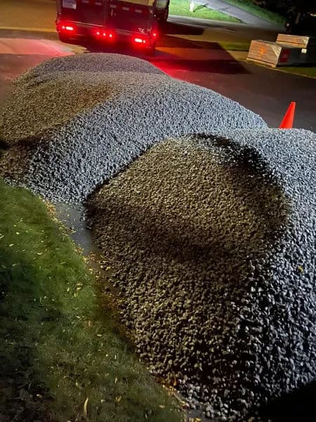 Pile of gravel covering a parked car at night, orange cone visible nearby.