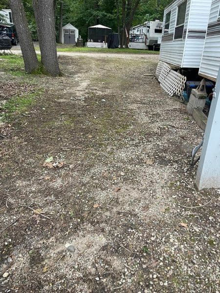 Gravel pathway in a wooded area with RVs and a shaded seating area in the background.