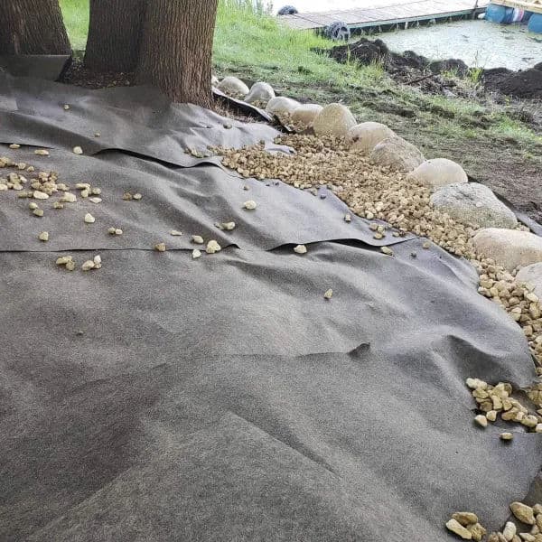 Landscaping fabric with stones along the edge of a water feature in a garden setting.