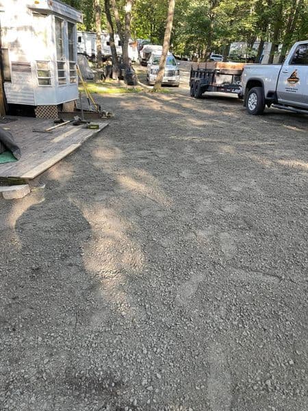 Gravel campsite area with RVs and a truck parked in a wooded setting.