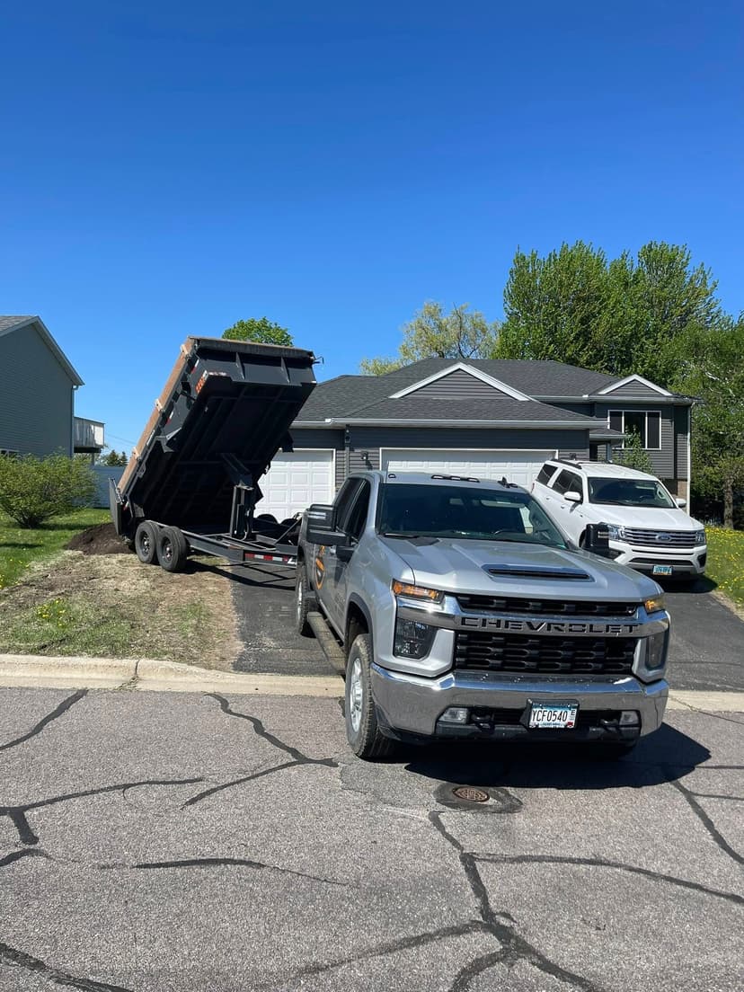 Chevrolet truck parked beside a dump trailer at a residential home on a sunny day.