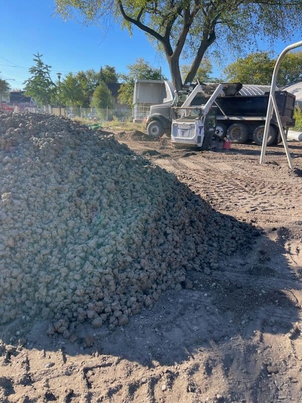 Piled gravel at a construction site with a dump truck in the background.