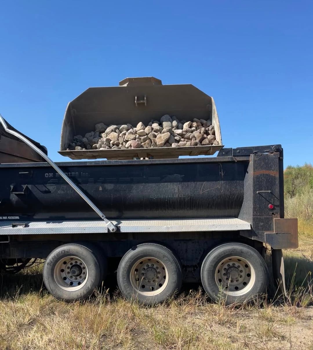 Dump truck unloading rocks at a construction site under a clear blue sky.