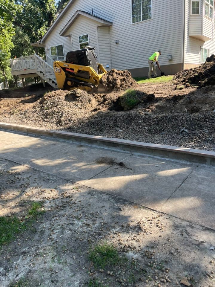 Construction site with mini skid steer and worker excavating soil near a house.