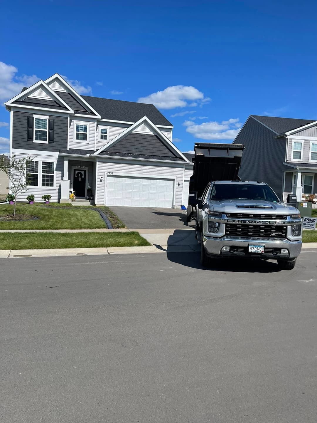 Modern house with a driveway and a dump truck parked in front on a sunny day.