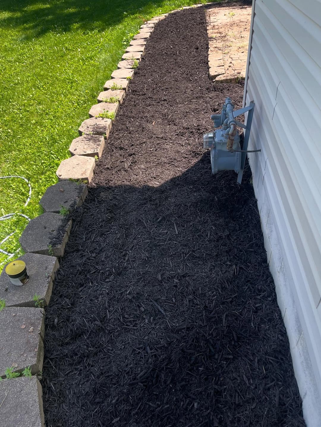 Freshly mulched garden path beside a house with stone edging and gas meter.