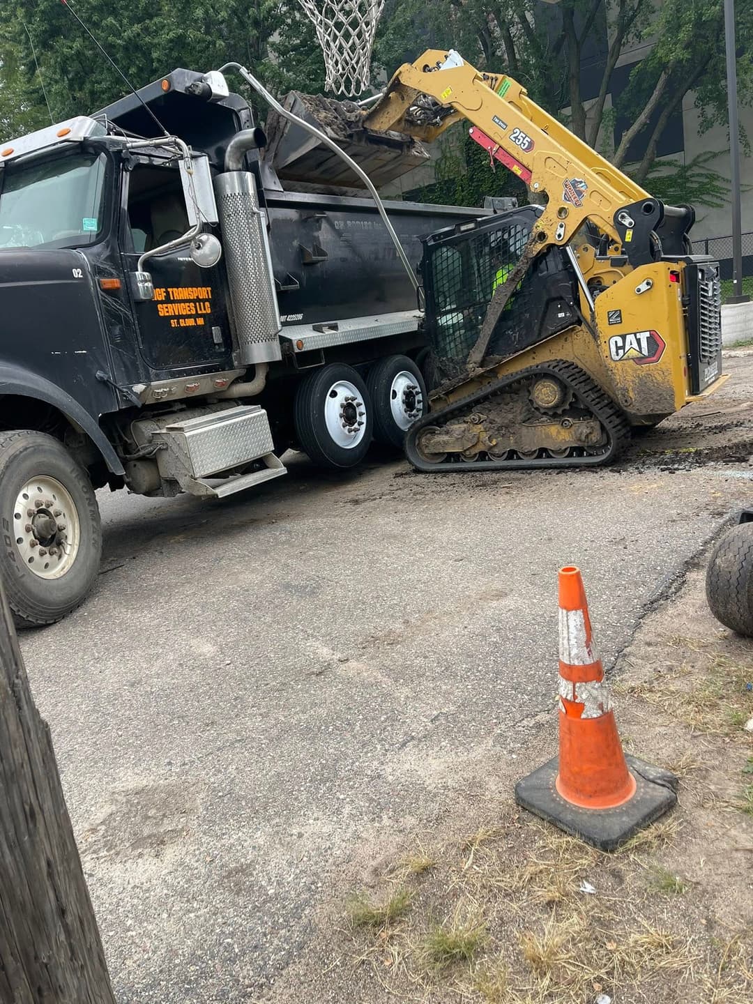 Dump truck and skid steer unloading debris near a basketball hoop at a construction site.