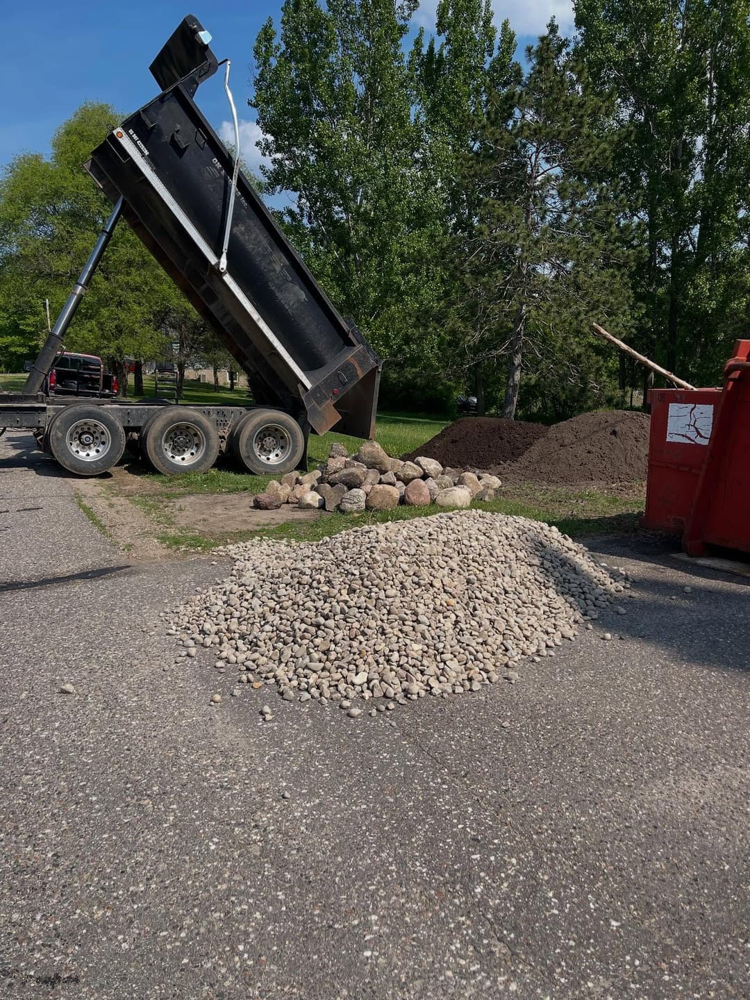 Dump truck unloading gravel and rocks at a construction site with trees in the background.