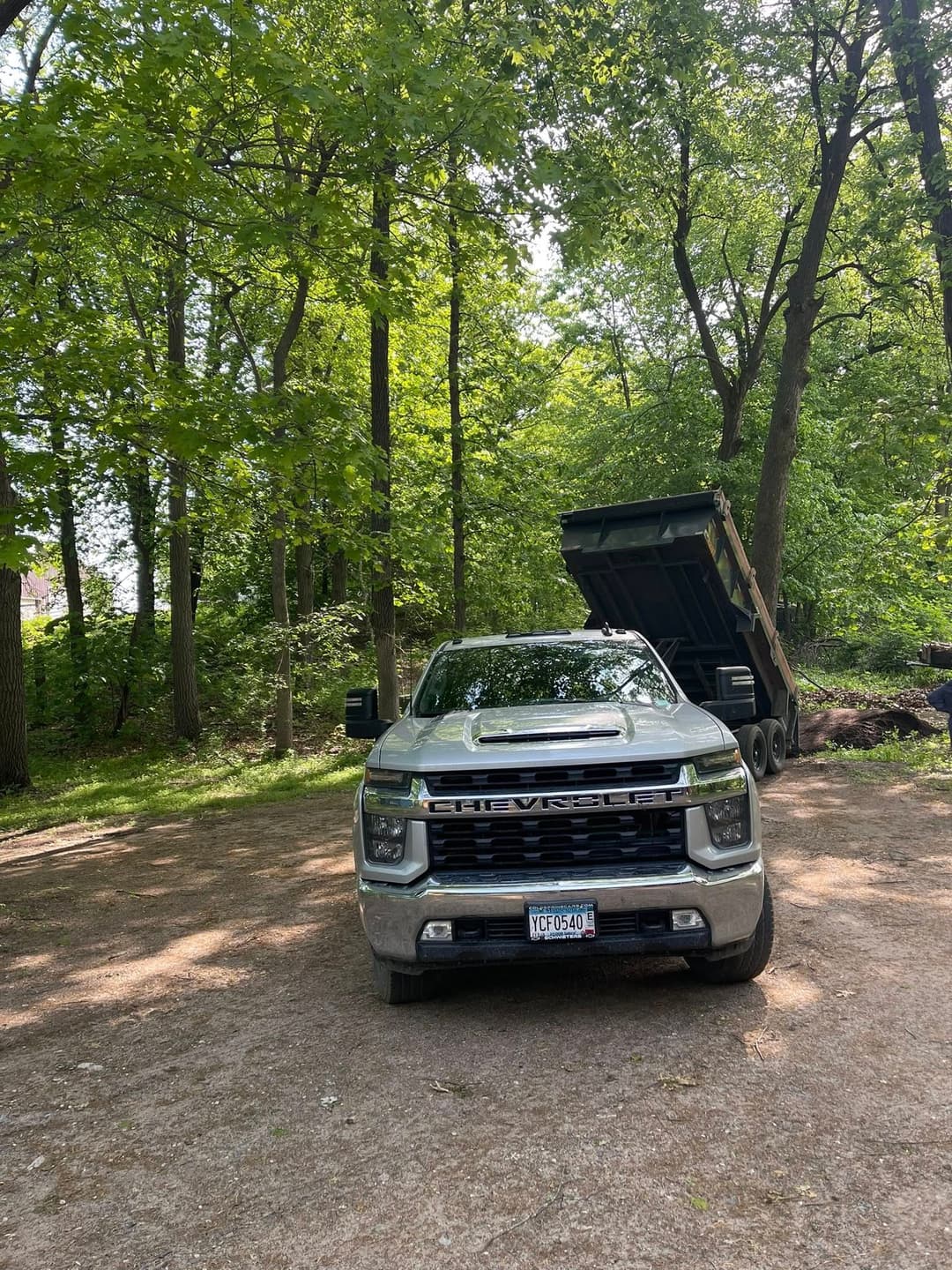 Chevrolet truck parked in a wooded area with a raised dump trailer in the background.