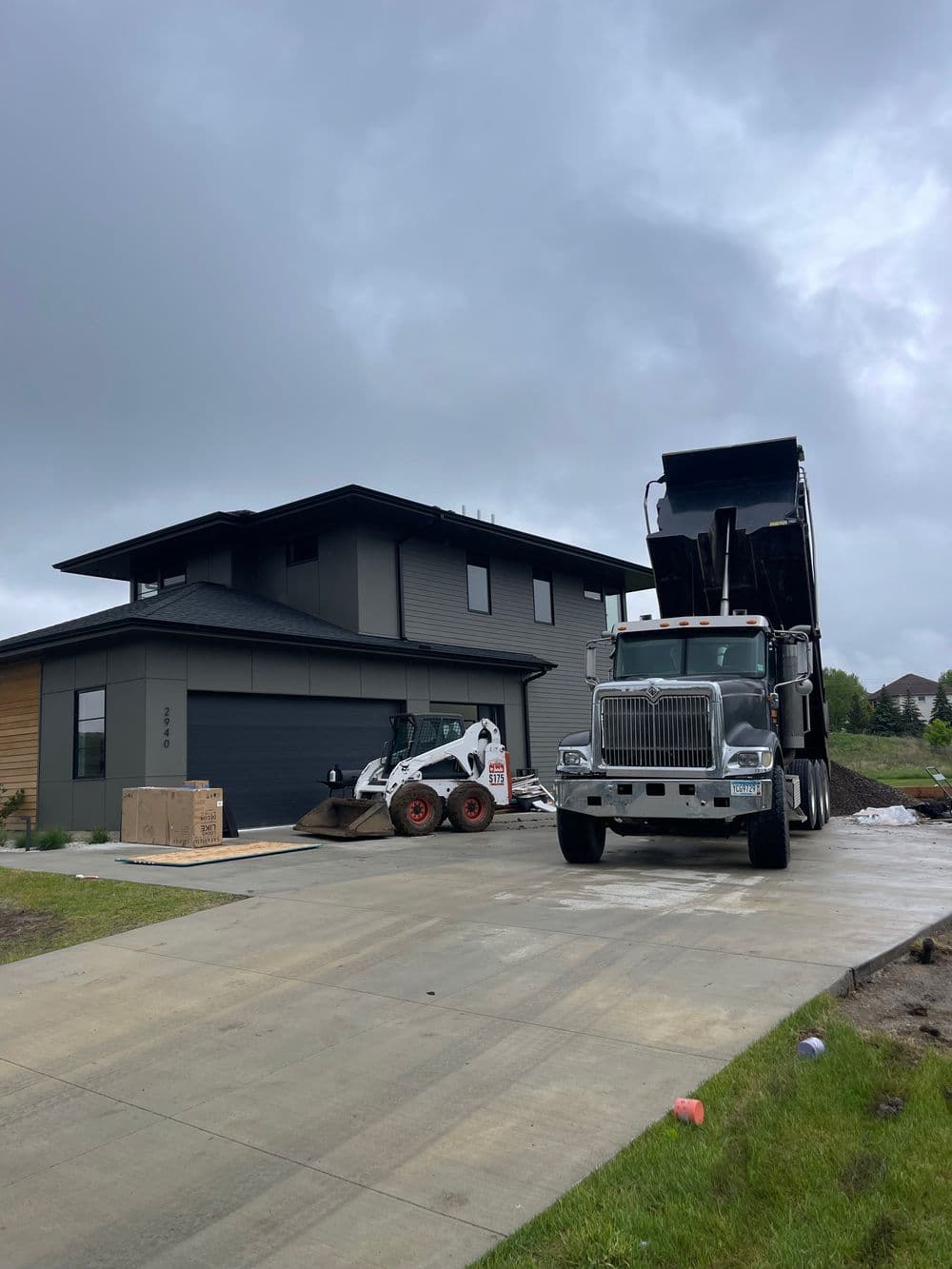 Dump truck unloading materials at modern house construction site with skid steer loader.