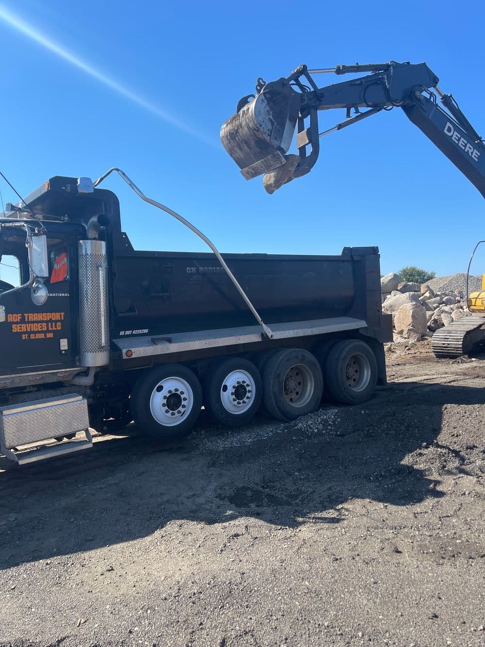 Dump truck being loaded with materials by a John Deere excavator on a construction site.