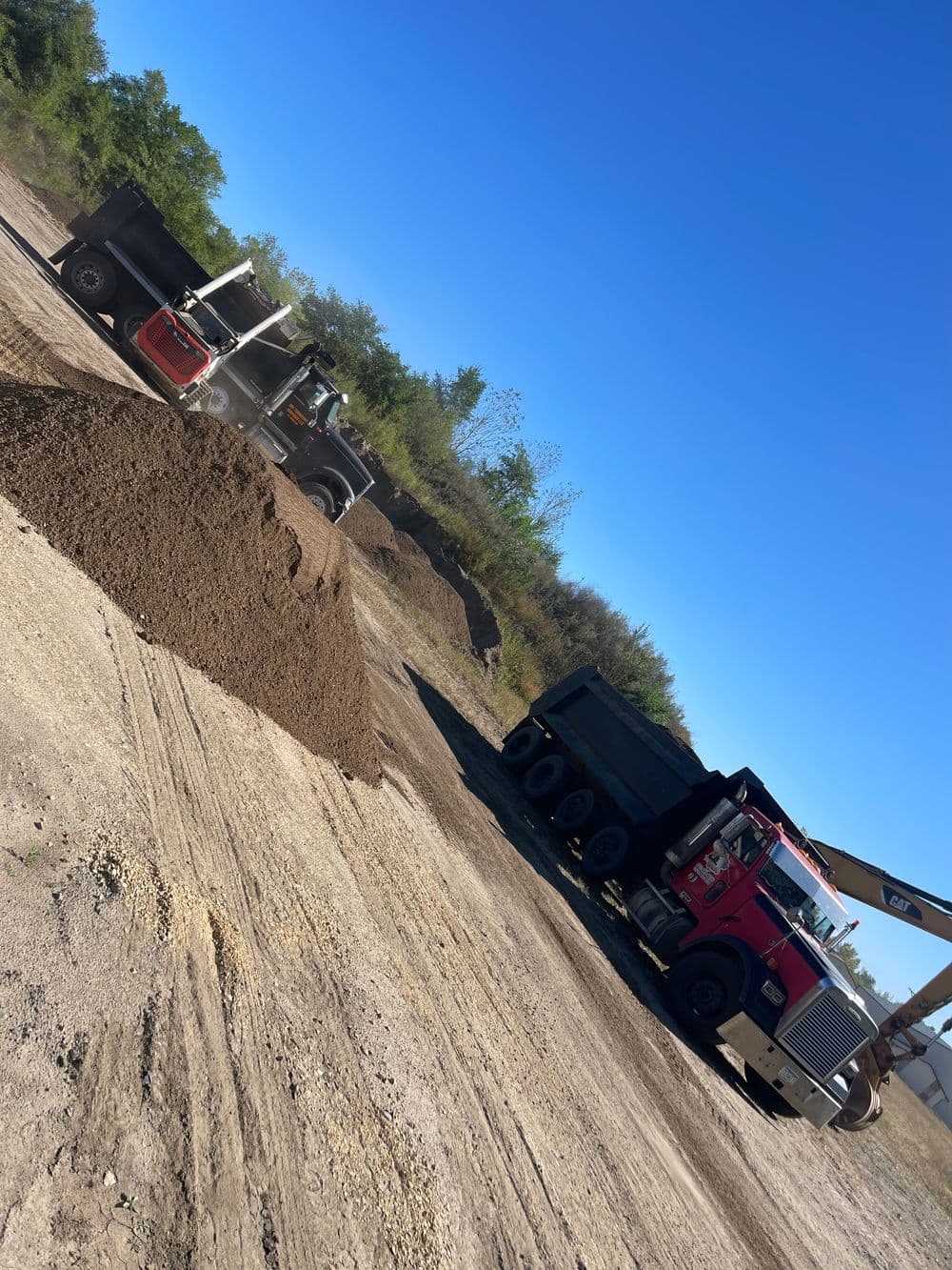 Construction site with dump trucks unloading dirt under a clear blue sky.