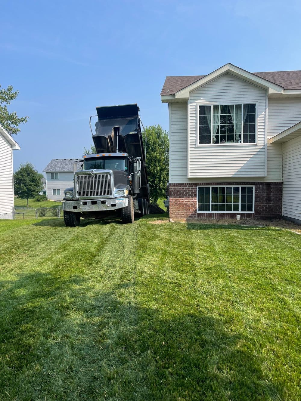 Dump truck unloading materials next to a well-maintained lawn and modern house.