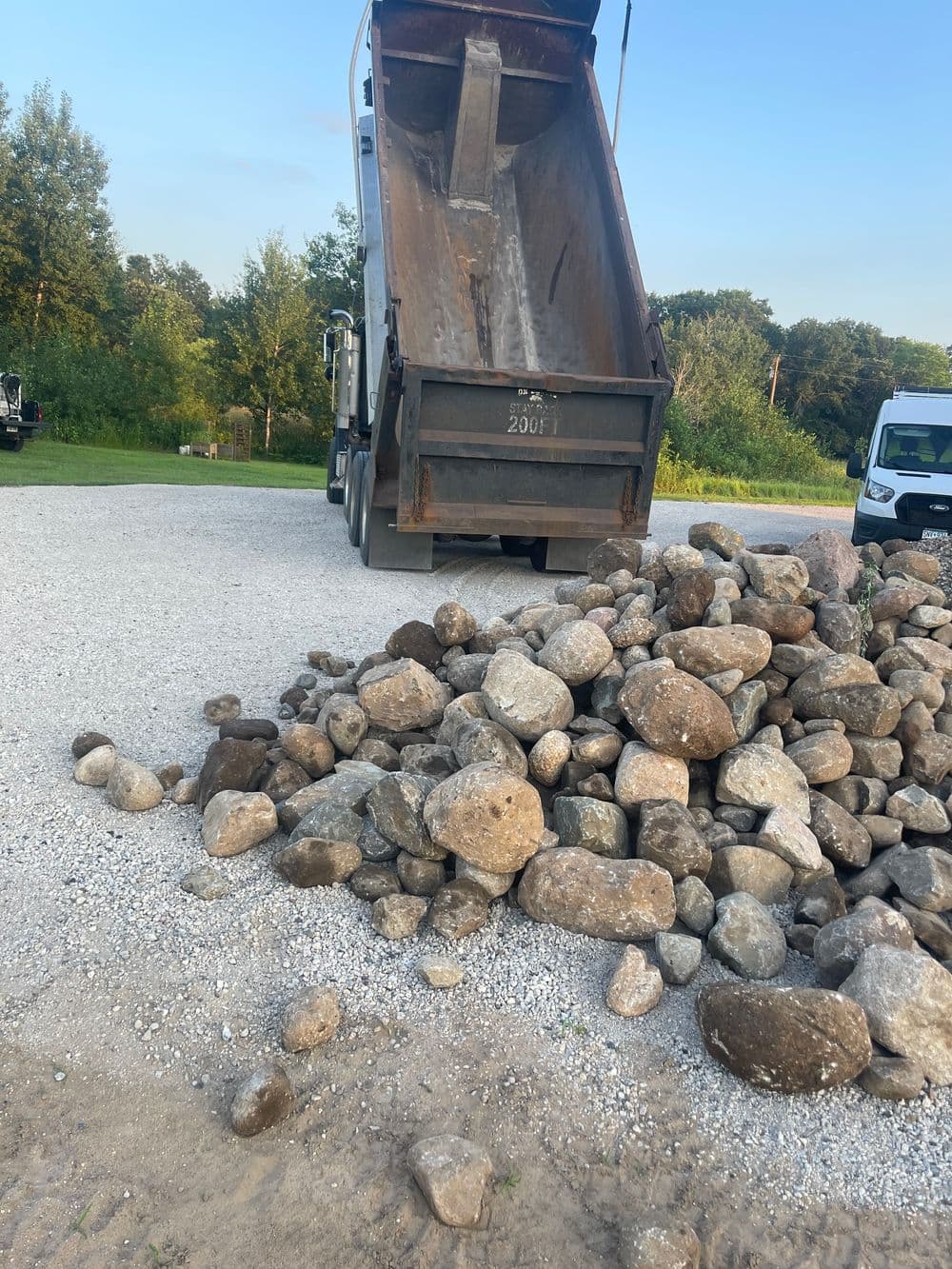 Truck unloading large rocks at a gravel site under a clear blue sky.