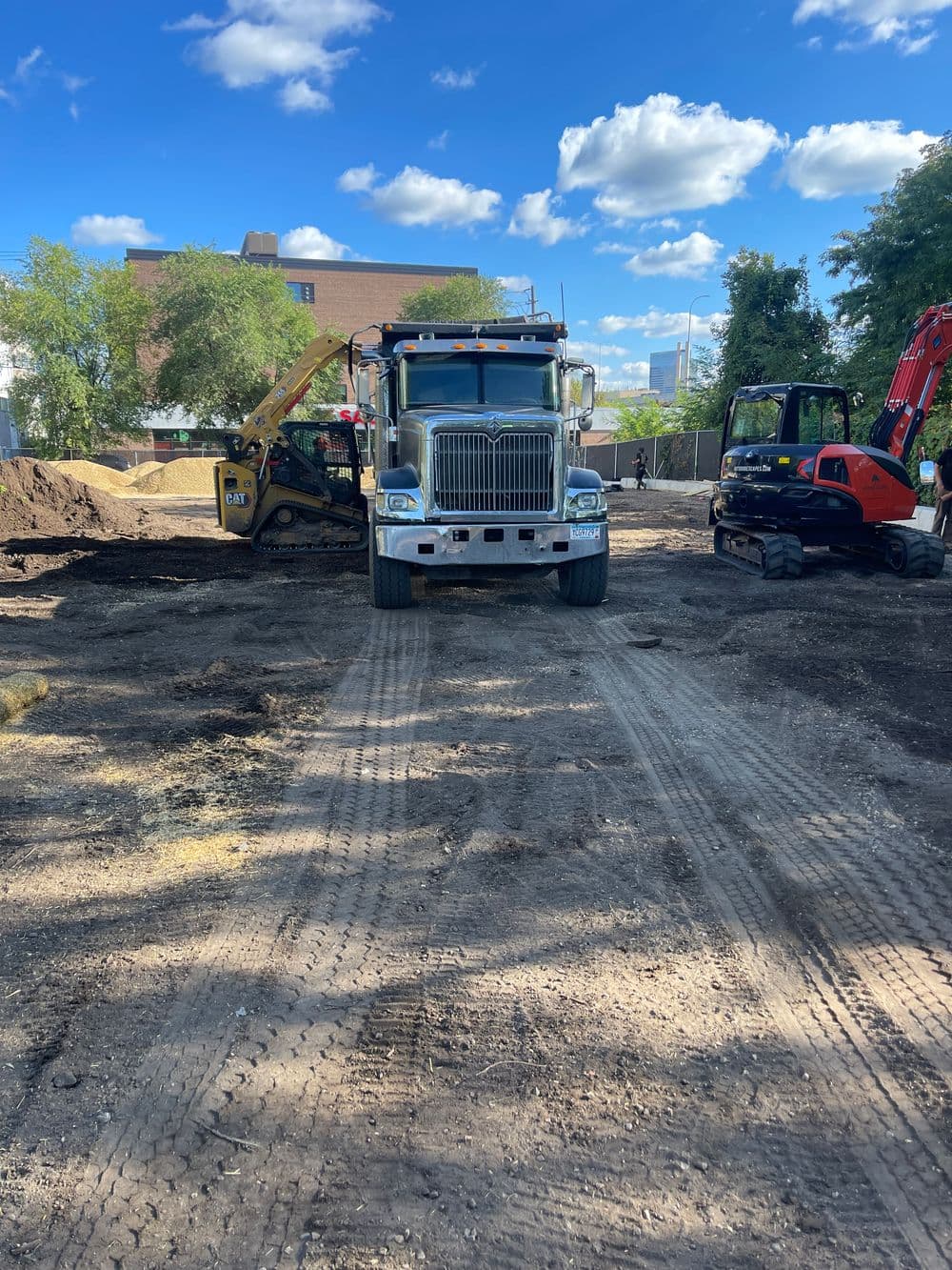 Construction site with heavy machinery, including a dump truck and excavators, under a clear blue sky.