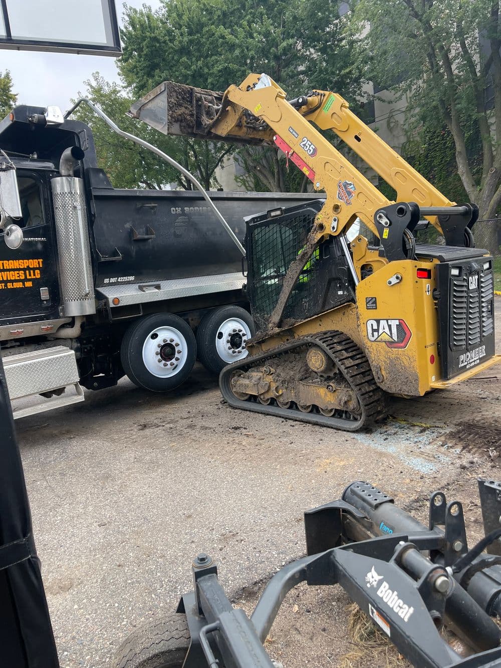 CAT skid steer loader unloading dirt into a black dump truck at a construction site.