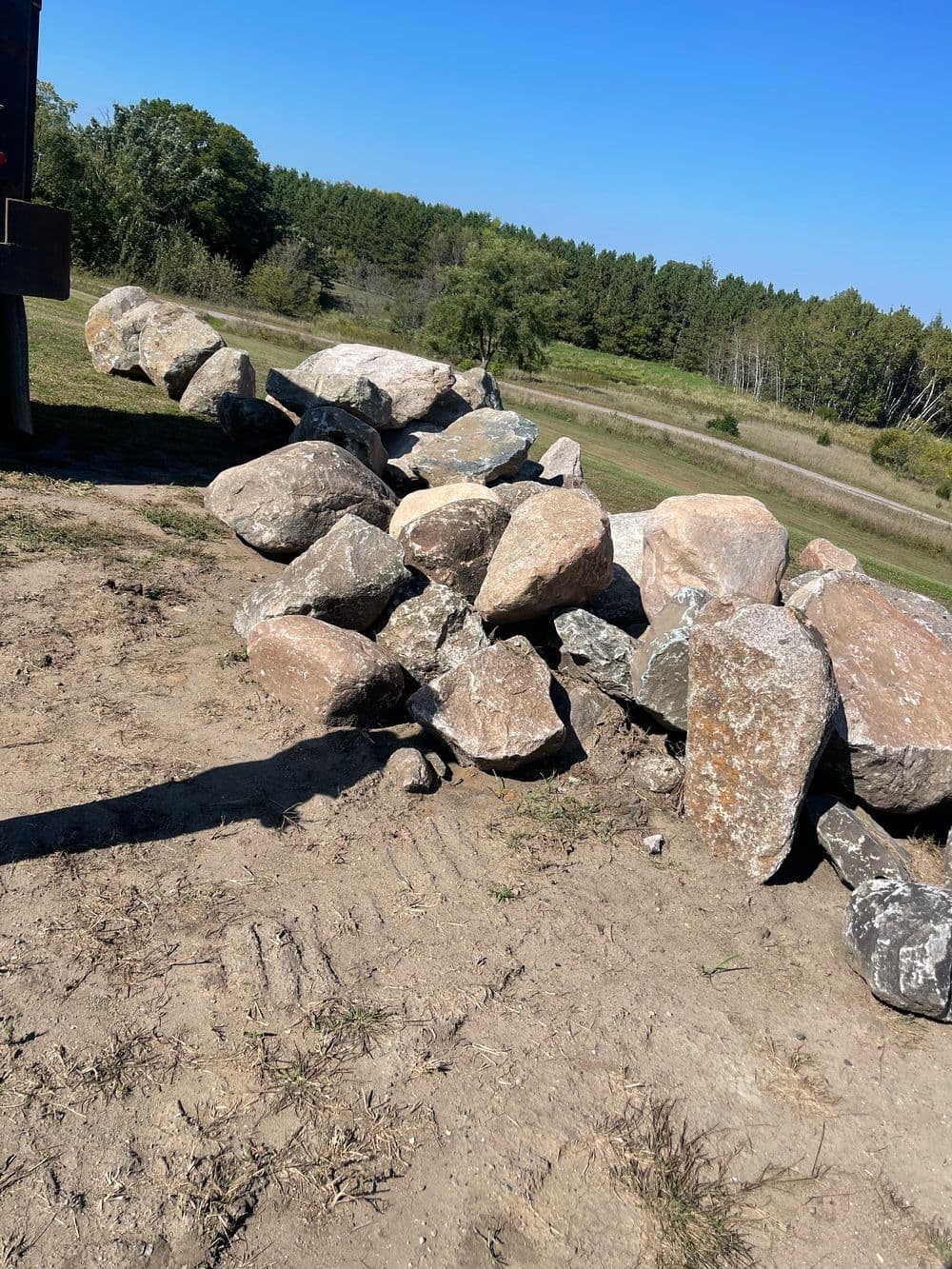 Rock formation along a dirt path with greenery and trees in the background on a sunny day.