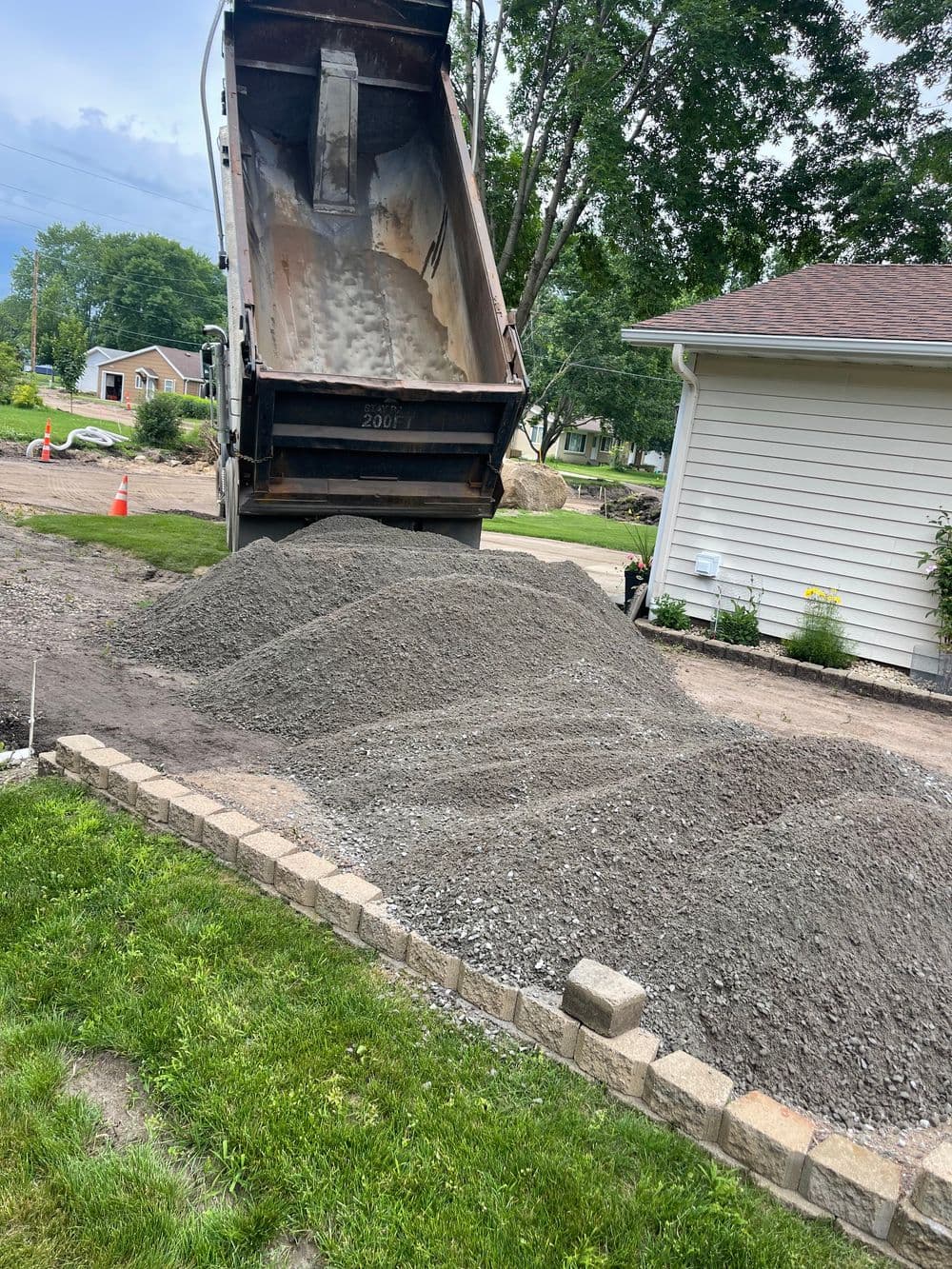 Dump truck unloading gravel for landscaping in a residential yard with a stone border.
