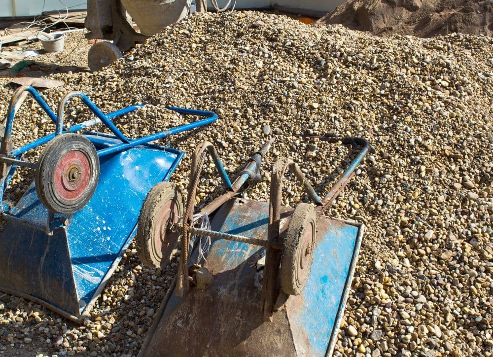 Two blue wheelbarrows on a gravel pile at a construction site.