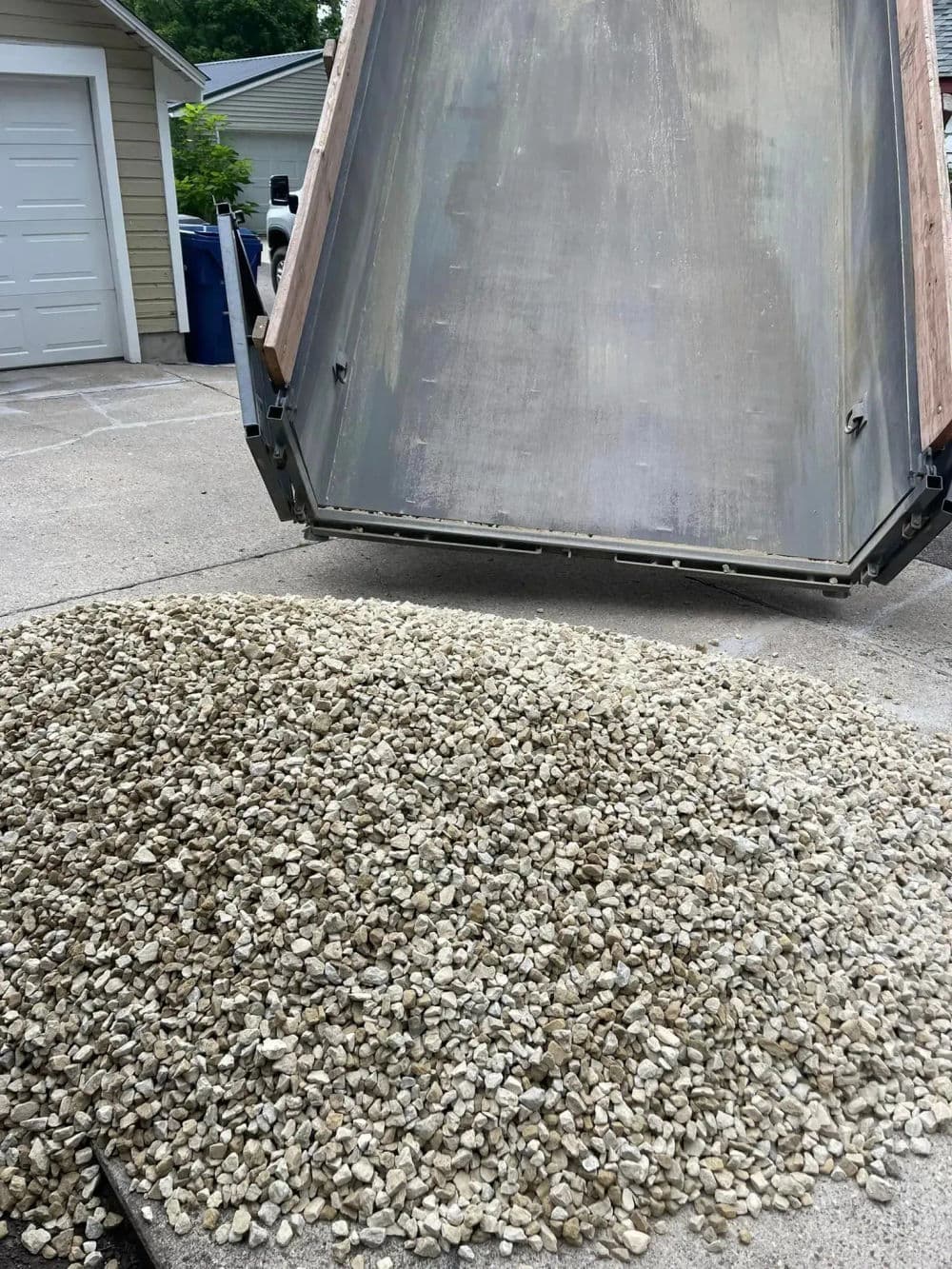 Dump truck unloading gravel on driveway, creating a pile of small stones.